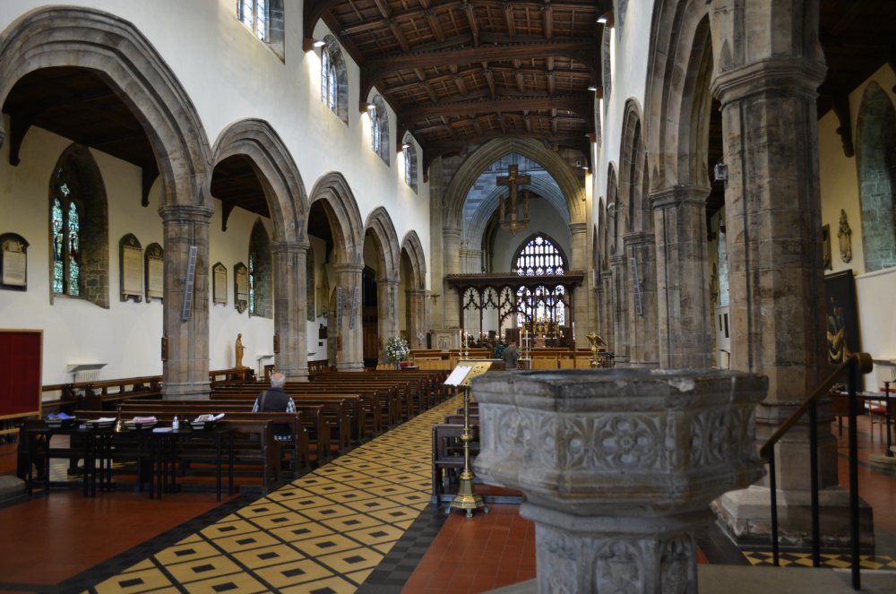 Looking east down the nave and on the right is the earl 15th century stone font engraved with the Diocesan Coat of Arms Saint Deiniol's Cathedral, Bangor, North Wales